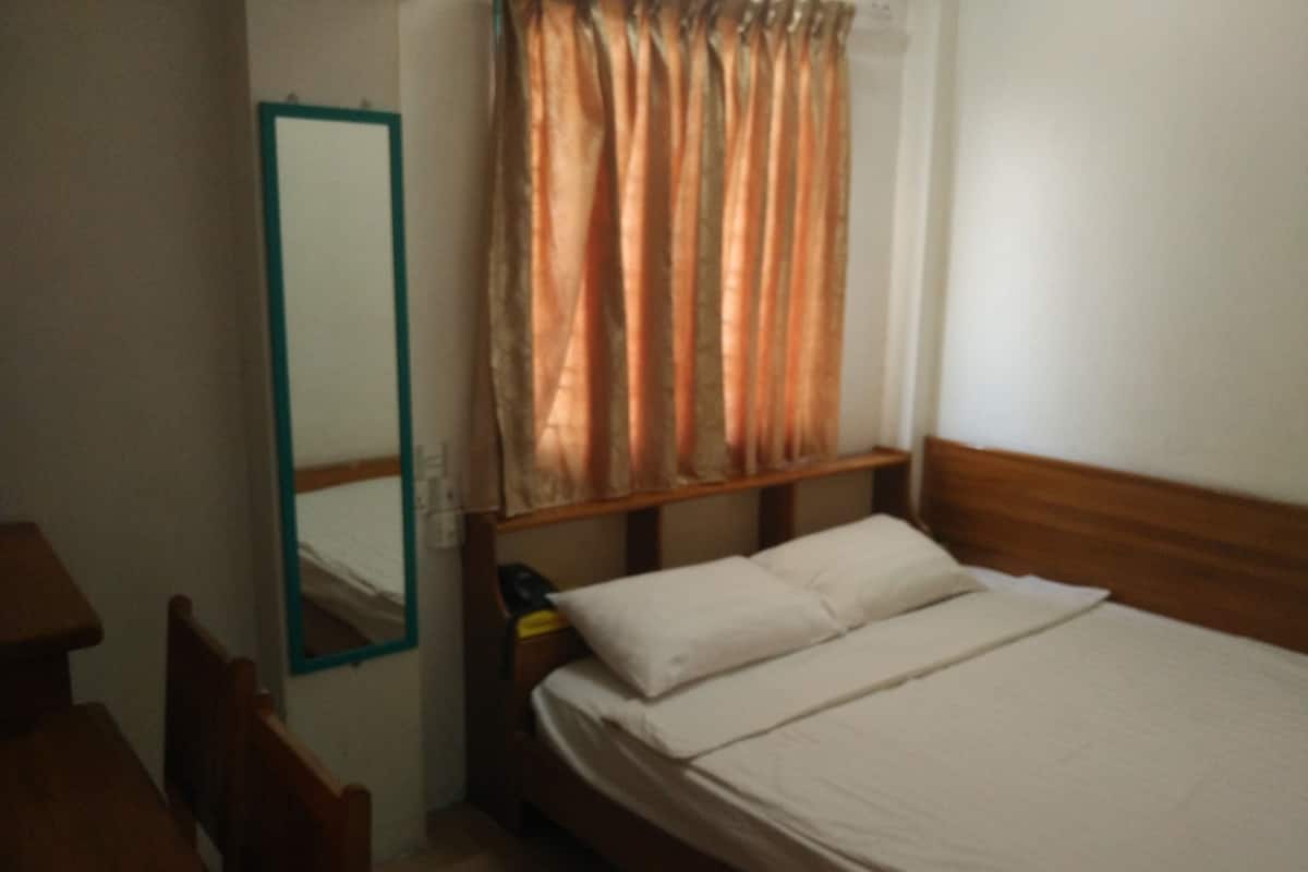 A bedroom with a wooden bed, a nightstand, a mirror, and a window with curtains.