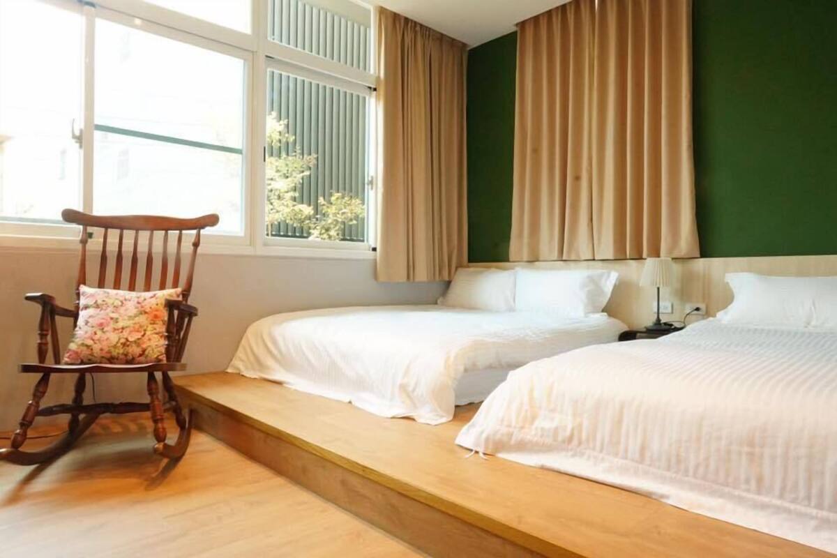 A bedroom with two beds, a rocking chair, and a window with curtains.