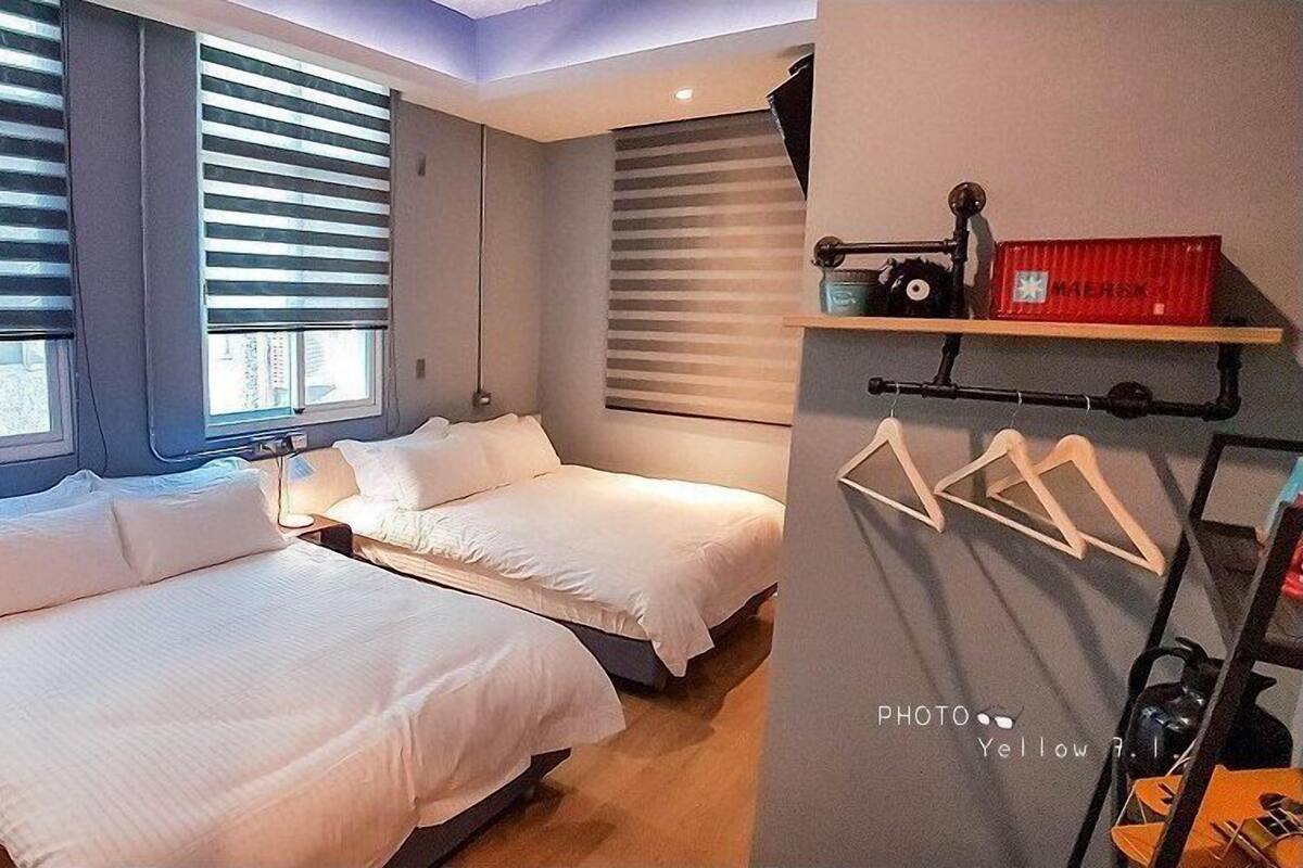 A modern hotel room with two beds, a TV, and a shelf with hangers.