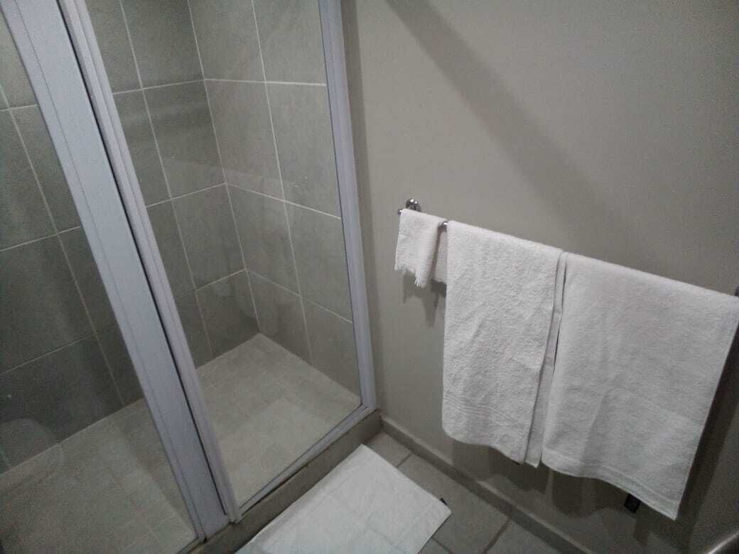 A bathroom with a glass shower enclosure, a towel rack with two white towels, and a small mat on the floor.