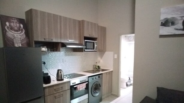 A compact kitchen with a refrigerator, microwave, stove, and washing machine. - Apartment In Rosebank Johannesburg (Johannesburg)