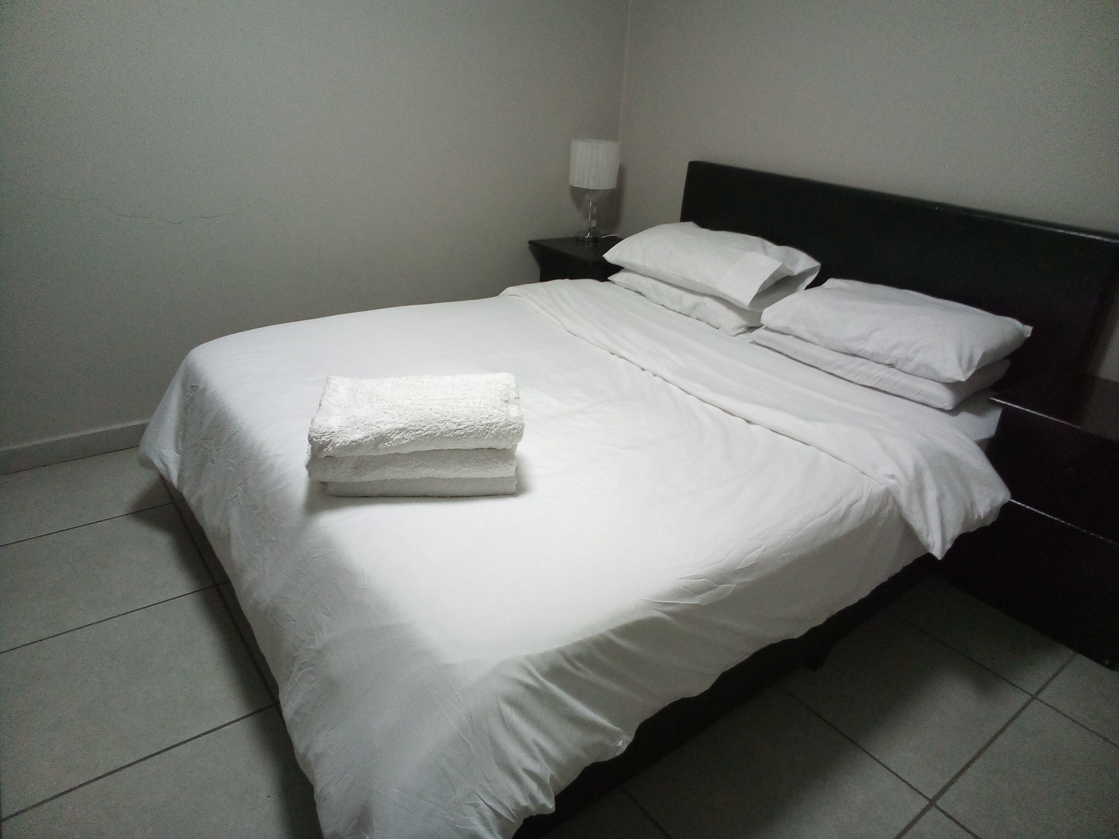 Un lit bien fait, avec des draps blancs et une serviette pliée posée sur le pied de lit.