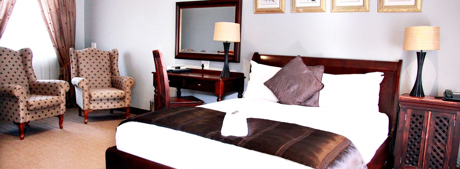 Habitación de hotel con una cama grande, dos sillones, un escritorio, un espejo y dos lámparas de noche.