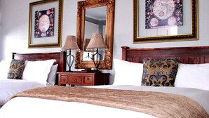 Una habitación de hotel con dos camas, cabeceros de madera, mesitas de noche con lámparas y obras de arte enmarcadas en las paredes.