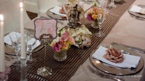 Una mesa de comedor dispuesta con velas blancas, centros de mesa florales y un candelabro de estilo antiguo.