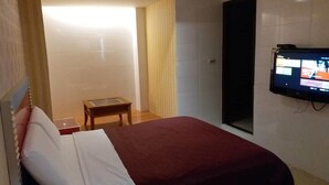 Hotelkamer met een bed, een kleine tafel, een aan de muur bevestigde televisie en een schuifdeur die leidt naar een andere kamer.
