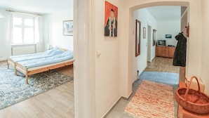 Un dormitorio con una cama, una ventana y un pasillo que lleva a una sala de estar con un televisor y un armario.
