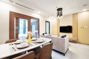 Un espace repas moderne avec une table dressée pour quatre personnes, un canapé et un téléviseur à écran plat fixé au mur.