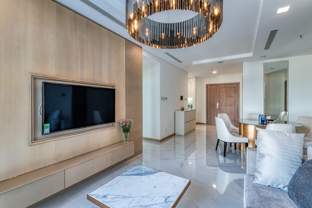 A modern living room with a flat-screen TV, a marble coffee table, a dining area with a white table and chairs, and a large mirror.