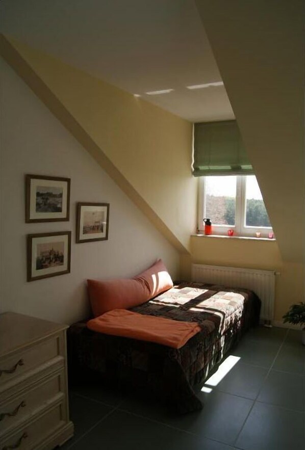 Un dormitorio con techo inclinado, una cama con cubrecama estampado, un aparador y una ventana con vistas al exterior.