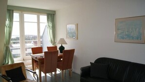 Ett rum med ett matbord, stolar, en svart soffa, en lampa och två tavlor på väggarna.