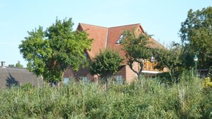 A house with a red roof, surrounded by trees and a body of water. - Blick auf Vilm (Putbus)