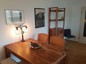 A wooden dining table with a plate of pinecones, a wall-mounted lamp, and two wicker chairs. - Blick auf Vilm (Putbus)