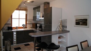 A modern kitchen with a central island, a dining area with two chairs, and a large window providing natural light. - Blick auf Vilm (Putbus)