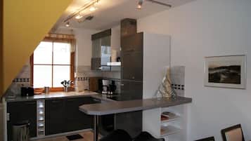 Cozinha moderna com ilha central, área de jantar com duas cadeiras e uma janela grande que proporciona luz natural.