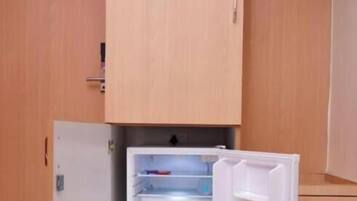 A compact kitchen with a built-in refrigerator, a wooden cabinet above, and a small countertop.