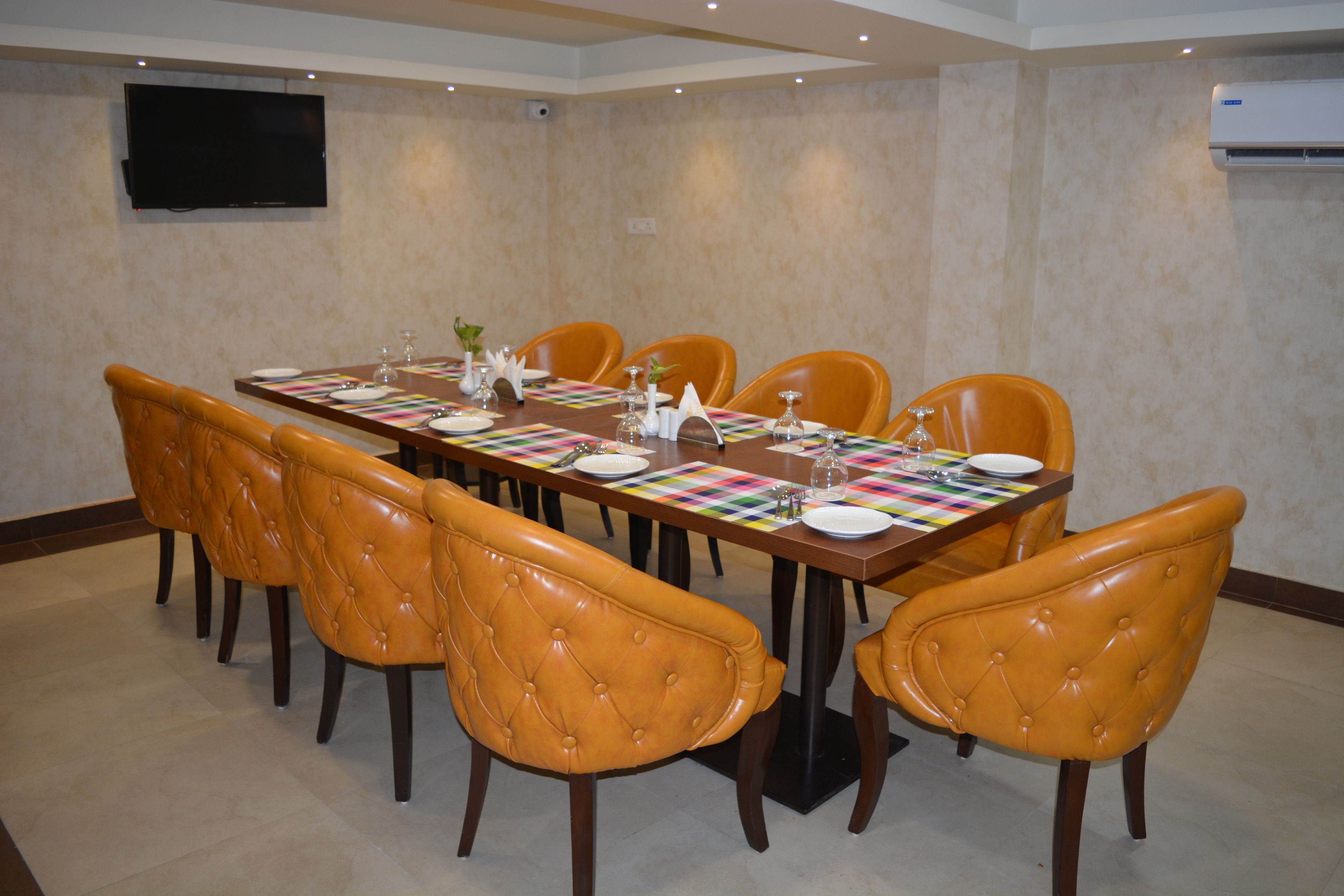 A conference room with a long table, six chairs, and a flat-screen TV on the wall.