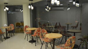 Un espace repas moderne avec des tables rondes et des chaises à motifs, agrémenté d’une cloison en verre et d’un éclairage suspendu.