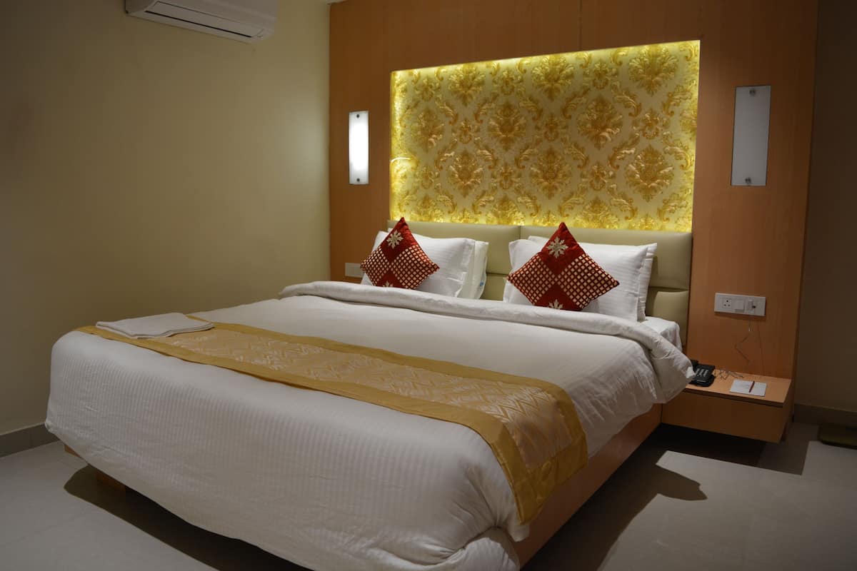 A hotel room with a large bed, a bedside table with a phone and papers, and a wall-mounted air conditioning unit.