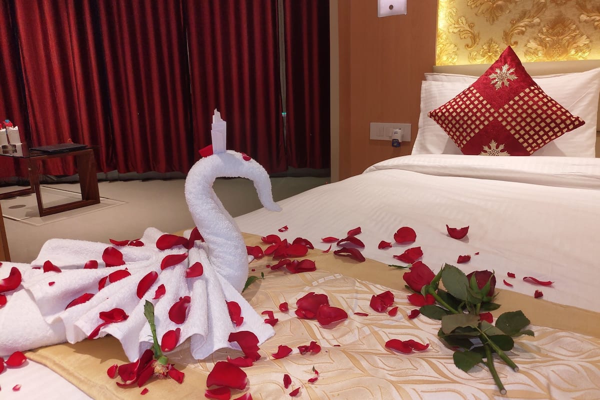 A hotel room with a bed, red curtains, and a decorative swan towel.