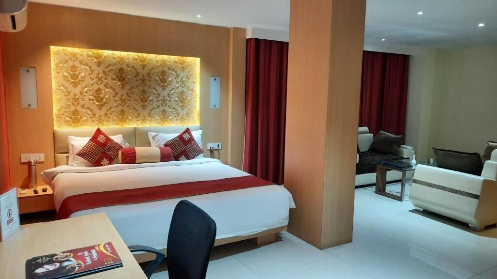 Hotellihuone, jossa on suuri sänky, työpöytä tuolilla, sohva ja punainen verho.