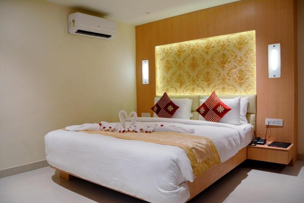 Una habitación de hotel con una cama grande, un cabecero con panel de luz, una mesita de noche con teléfono y lámpara, y un equipo de aire acondicionado en la pared.