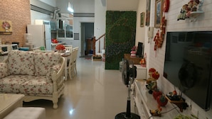 Una sala moderna con sofá, mesa de comedor y sillas. Hay una chimenea con adornos y un televisor. Se ve una cocina al fondo.