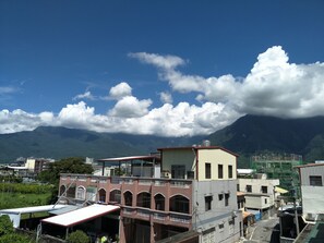 A multi-story building with a flat roof and a balcony, surrounded by other buildings and mountains in the background.