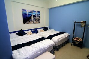A hotel room with two beds, a blue wall, and a painting of a coastal scene.