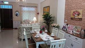 Un comedor con una mesa de madera, sillas blancas, un sofá floral y una mesa de comedor con tazas y un jarrón.