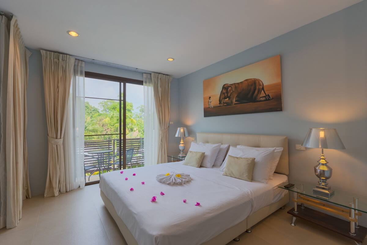A hotel room with a large bed, a balcony with a view, and a painting on the wall.