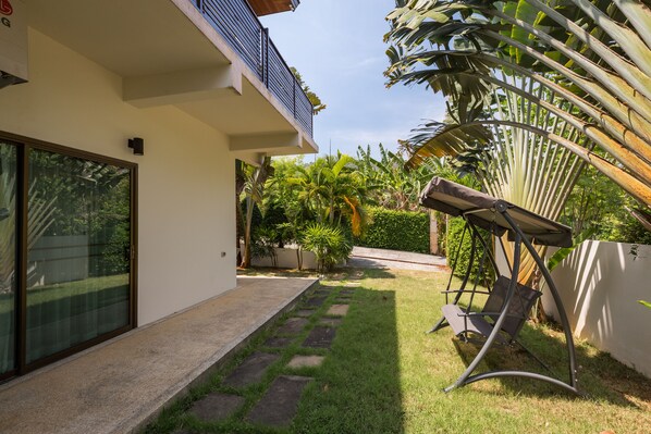 Uma casa moderna com porta de vidro, um pequeno jardim com cadeira de balanço e uma palmeira.