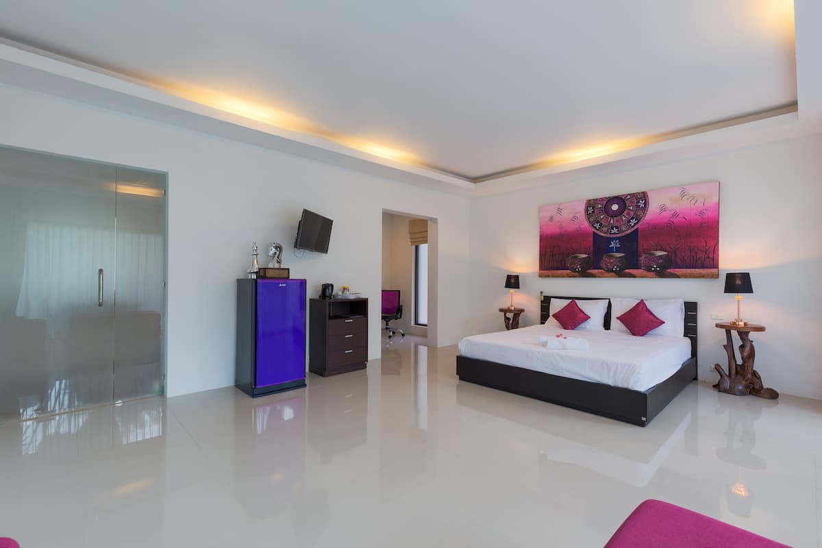 A modern hotel room with a large bed, a flat-screen TV, a desk with a computer, and a glass partition.