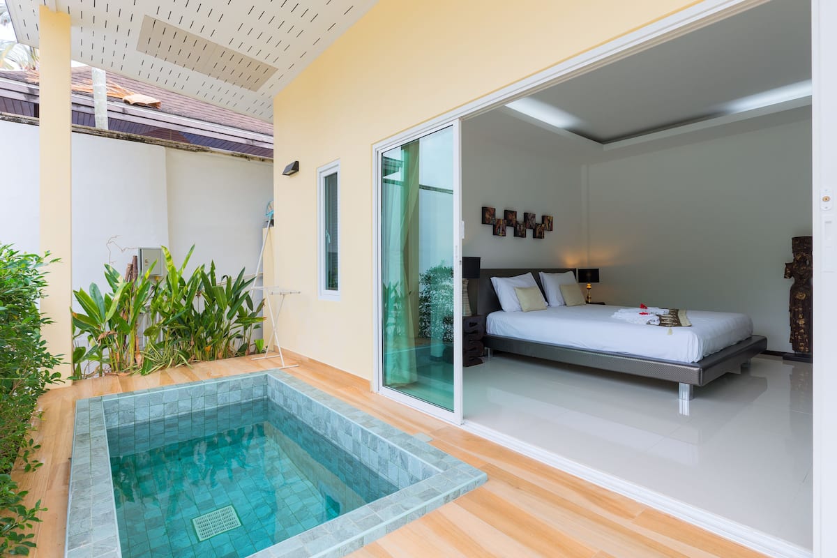 A modern bedroom with a large bed, a glass door leading to a balcony, and a small pool area.