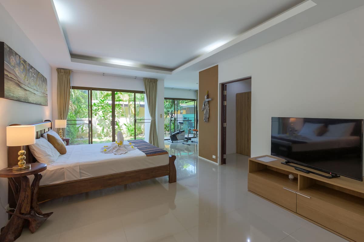 A modern hotel room with a large bed, a TV, and a balcony with a view of greenery.