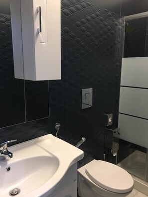 Een moderne badkamer met een wit wastafelmeubel, toilet en een douchecabine van glas.