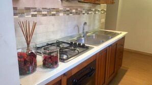 A kitchen with a gas stove, double sink, and wooden cabinets. - Il Cuore di Napoli (Naples)