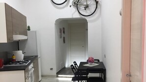 A compact kitchen with a dining area, a refrigerator, a stove, and a bicycle mounted on the wall. - Il Cuore di Napoli (Naples)