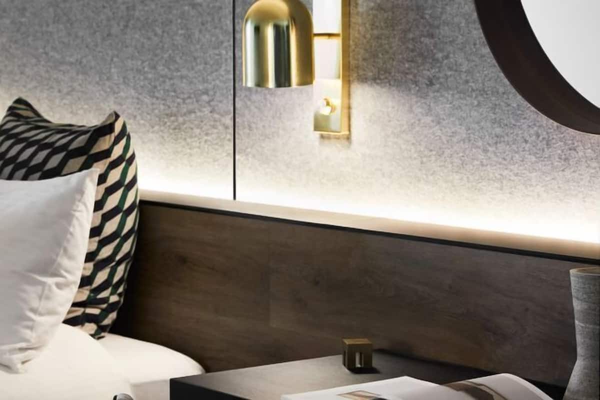 Ett modernt hotellrum med en säng, ett sängbord, en väggmonterad lampa och en dekorativ vas.