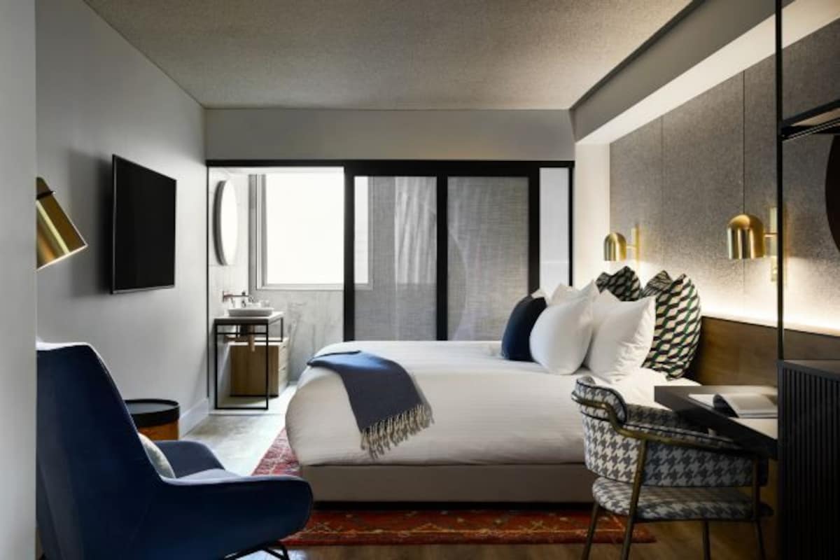 Una habitación de hotel moderna con una cama grande, un escritorio, una silla, un televisor y una ventana con cortinas.