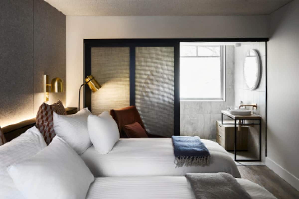 Ett modernt hotellrum med en stor säng, ett skrivbord, en stol, ett fönster och ett badrum.