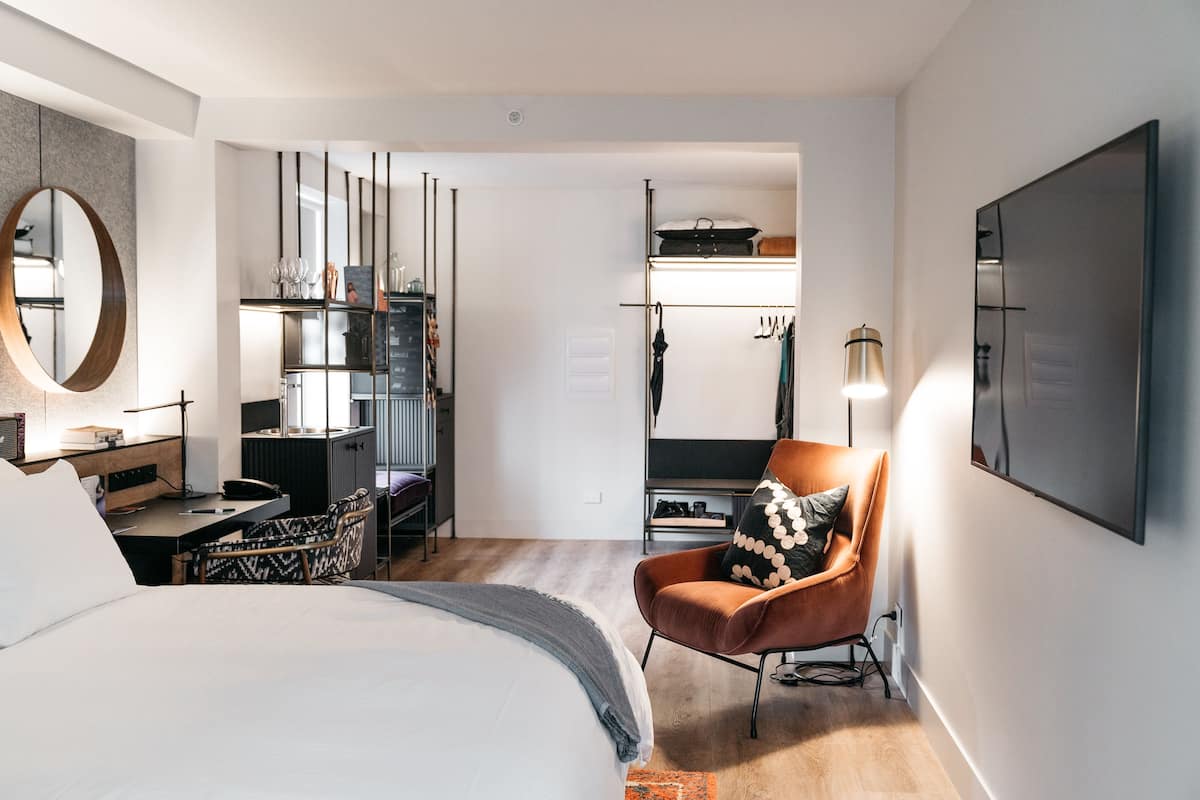 Ett modernt hotellrum med en stor säng, ett skrivbord, en stol, en garderob och en spegel.
