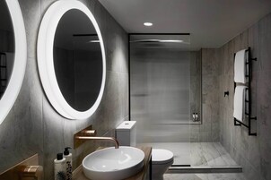 Een moderne badkamer met een grote, ovale spiegel, een rond wastafel, toilet en een douchehoek.