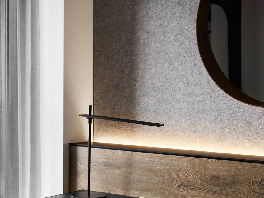 Moderni hotellihuone, jossa on puinen työpöytä, ruutukuviollinen tuoli, pyöreä peili ja kuvioitu seinä.