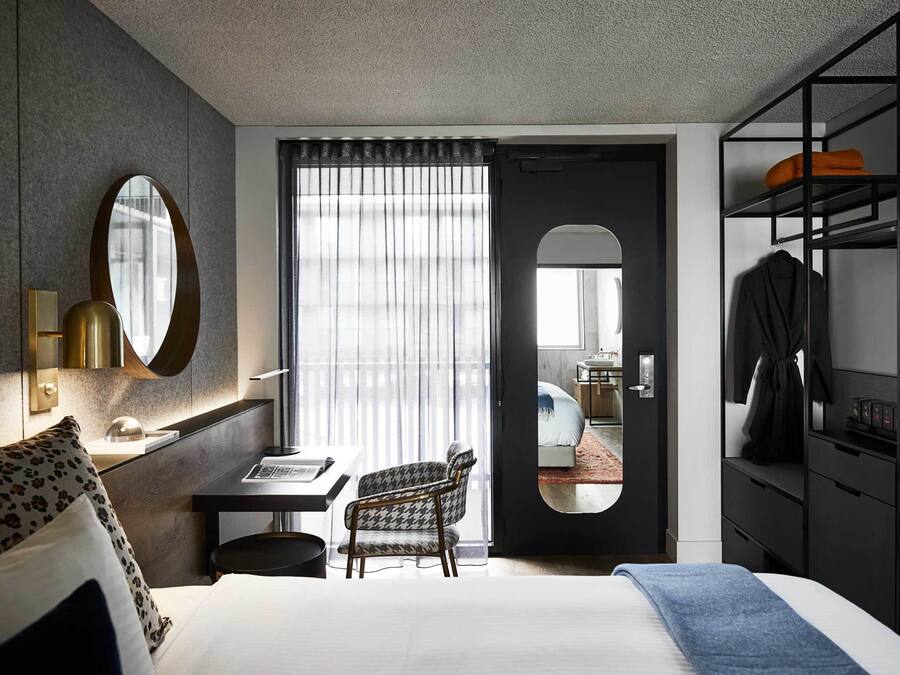 Una habitación de hotel con cama, escritorio, silla, armario y espejo.