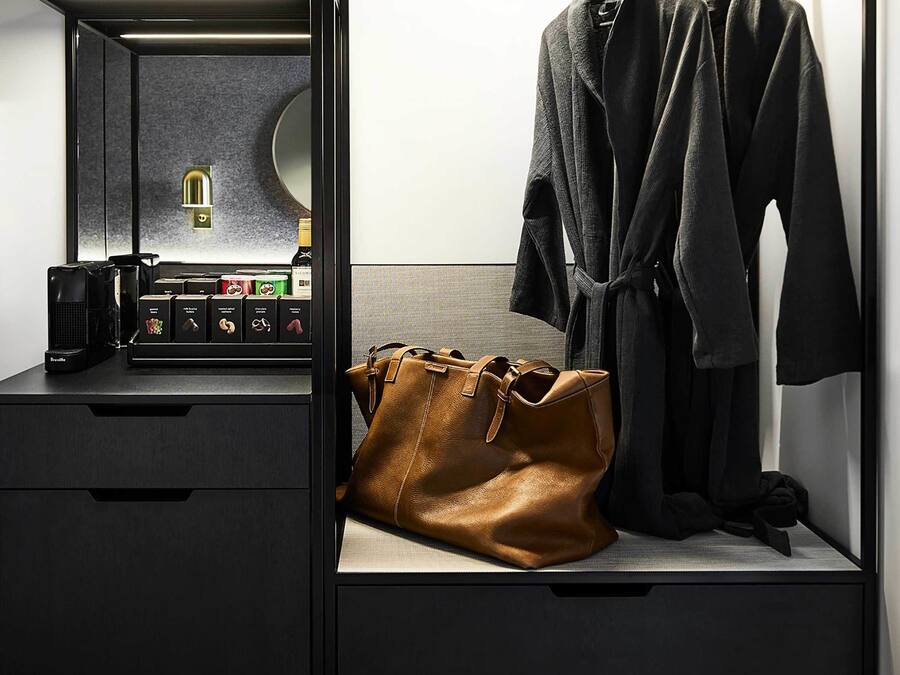 A modern, compact room with a built-in wardrobe, a vanity with a mirror, and a coffee machine.