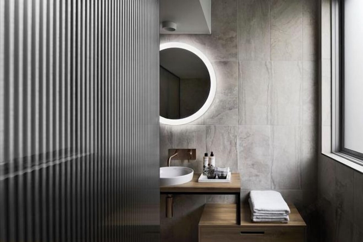 A modern bathroom with a round mirror, a wooden vanity, and a large window.