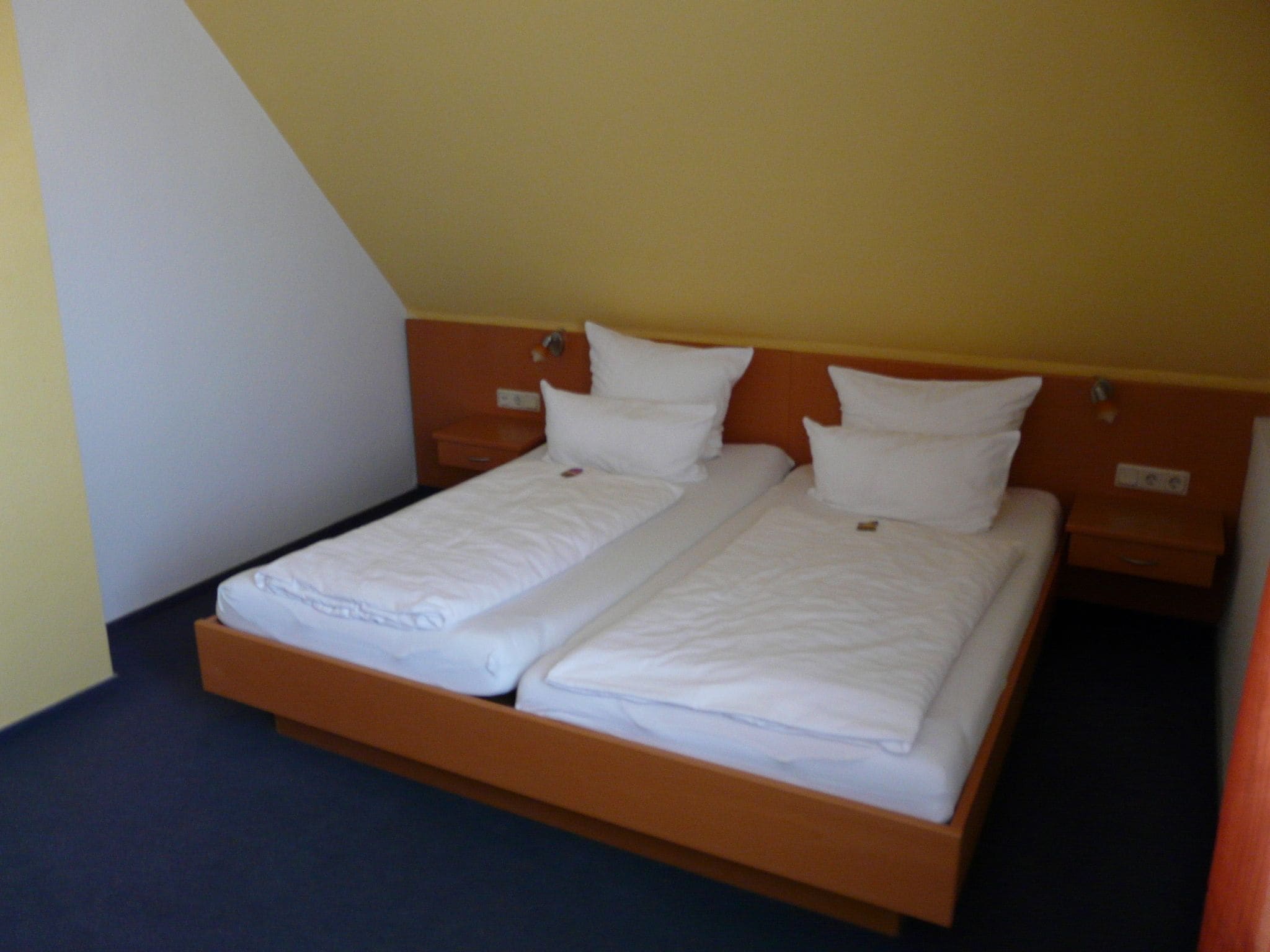 A single bed with a wooden frame and white bedding in a room with yellow walls and a dark floor.