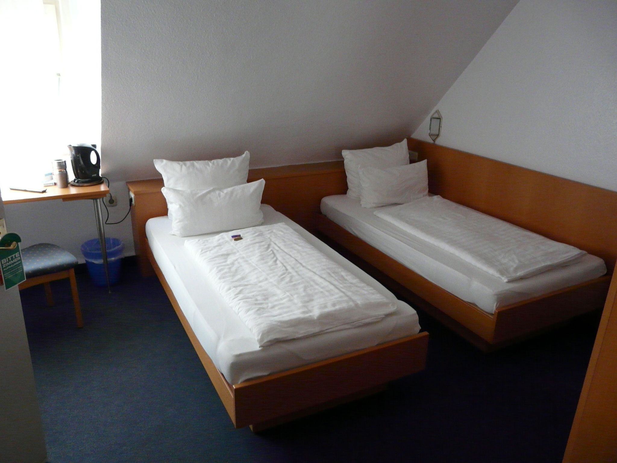 A room with two single beds, a desk with a kettle, and a chair.