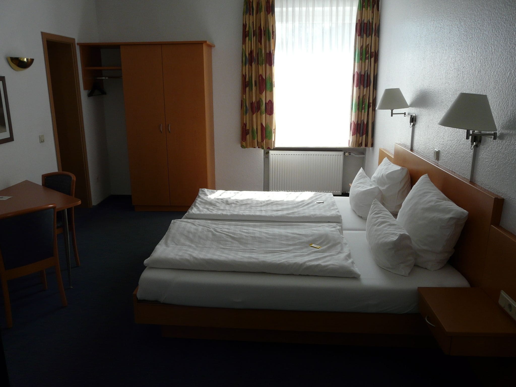 Een hotelkamer met een tweepersoonsbed, een bureau, een kledingkast en twee bedlampjes.